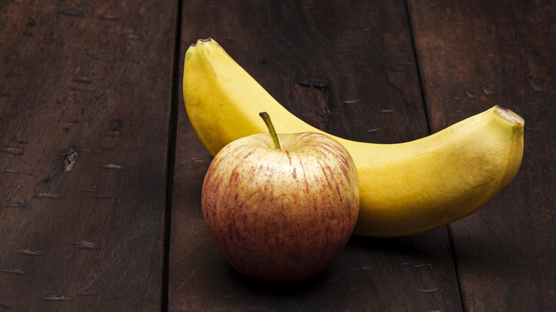 An apple and a banana on a wooden surface