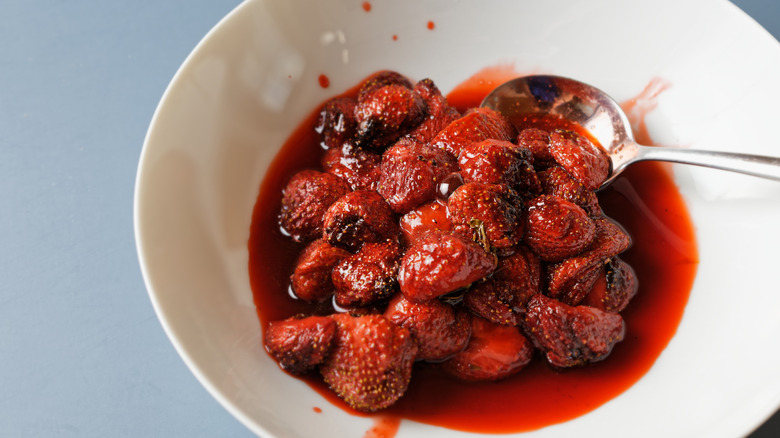 Roasted strawberries in a white bowl with a spoon beside them