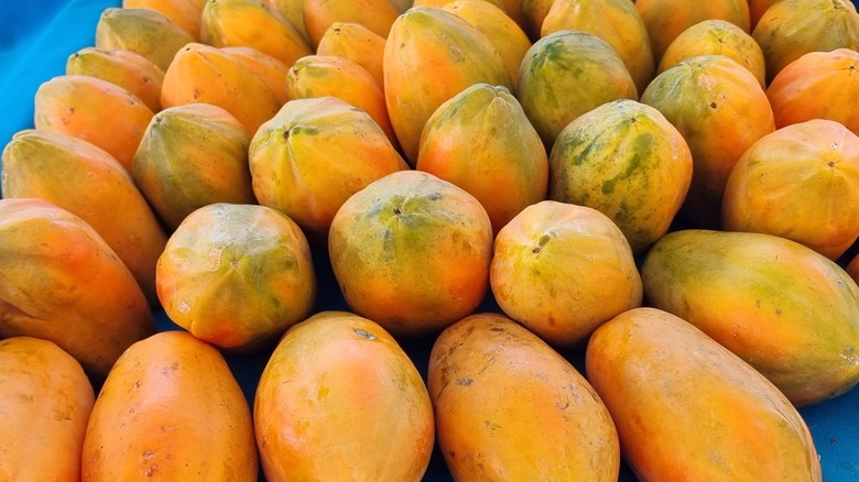 A vibrant and colorful close-up shot of a large pile of whole papayas