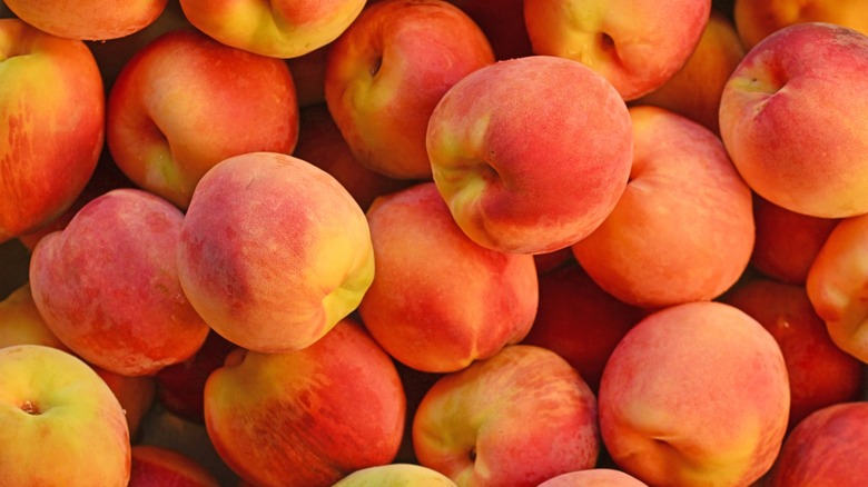 A bunch of whole peaches are piled on top of each other
