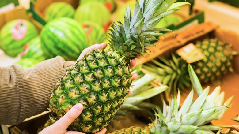 Hands holding a fresh tropical pineapple in a market setting