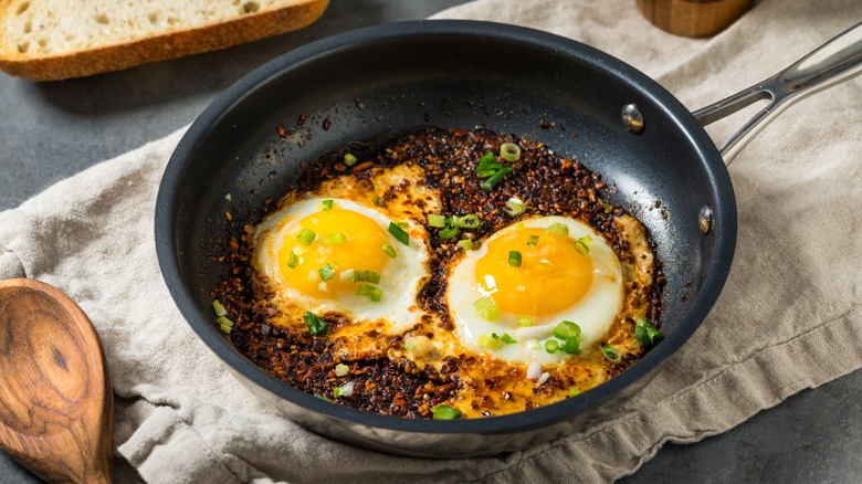 Two eggs, chili crisp, and green onion in a frying pan on a towel