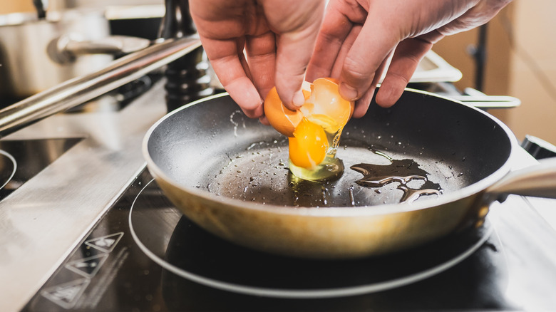 Hands cracking an egg into a frying pan
