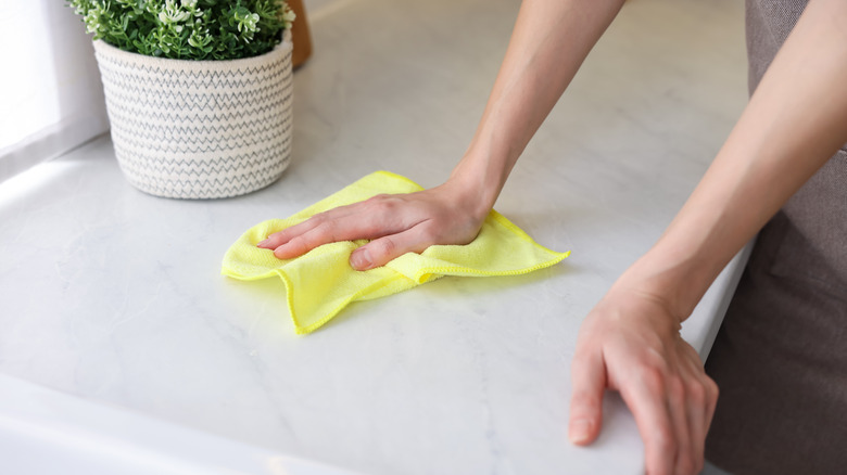 A close-up of hands wiping a countertop with microfiber cloth in kitchen.