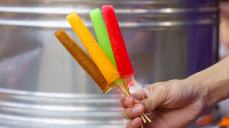 A person holding up four different flavored popsicles.