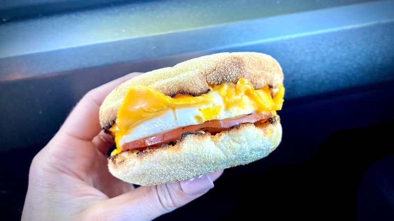 A McMuffin with a round white egg, cheese, and bacon in someone's hand