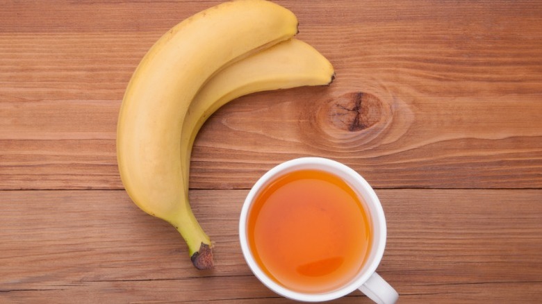 two bananas and a cup of orange-colored tea on a wooden counter