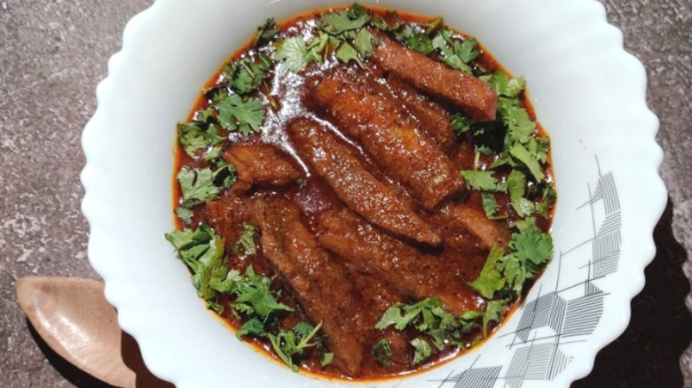 a white bowl on a counter filled with deep red-colored banana curry topped with cilantro