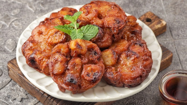 Indonesian-style banana fritters on a plate with herb garnish and a dark brown sauce on the side