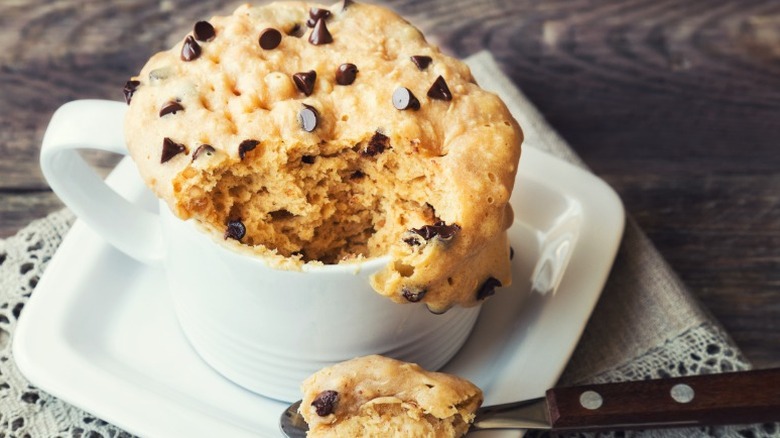 a chocolate chip mug cake with a spoonful taken out sits on a plate on a wooden table