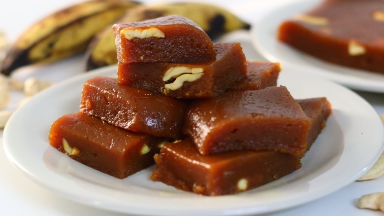 a stack of banana halwa with nuts on a plate with overripe bananas and more halwa in the background