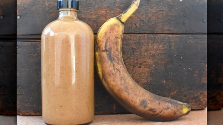 a large plastic bottle filled with homemade, reddish-brown banana ketchup next to a brown banana