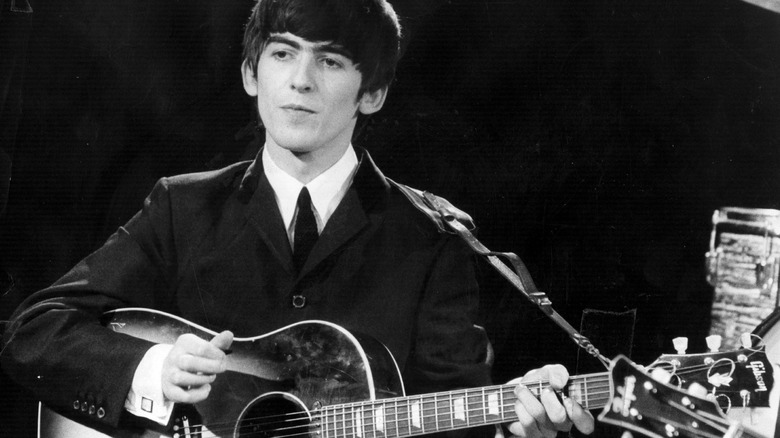 George Harrison of The Beatles playing guitar on stage.