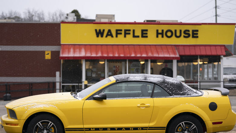 A Waffle House location with a bright yellow Mustang parked outside as snow is falling.