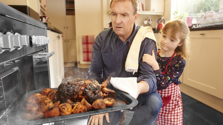 Person pulling burnt food from oven with child nearby