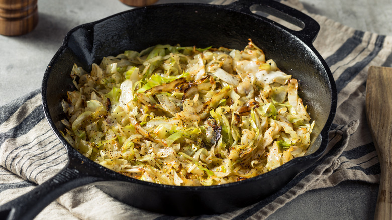 Sauteed green or white cabbage in a cast iron pan sitting on a striped dish cloth
