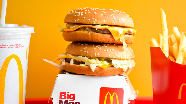 Two McDonald's burgers sitting on top of each other on a box with fries and a drink nearby.
