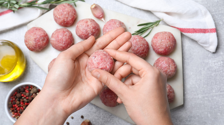 Hands making fresh raw meatballs at light gray table, top view.