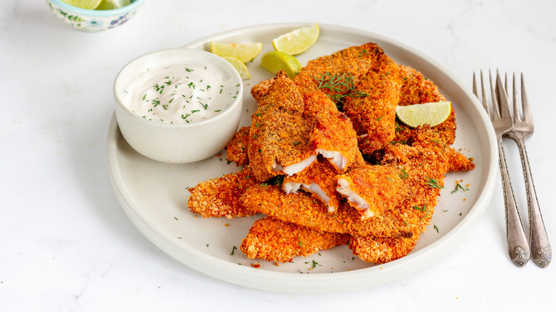 Fried crumbed fish on a plate with a dish of tartare sauce.