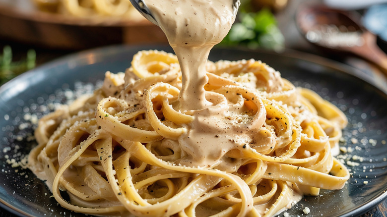 Fettuccine Alfredo with sauce pouring over the pasta.