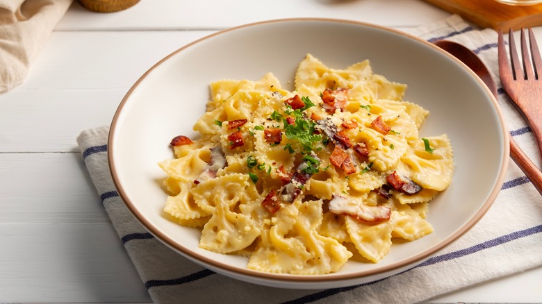 Bowtie pasta alfredo with bacon and parmesan on a white plate