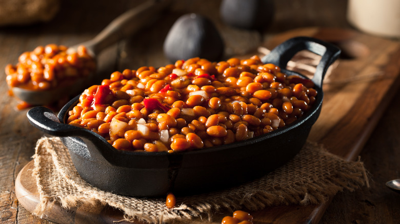 A cast iron pan of baked beans with onions and tomatoes on a wooden table