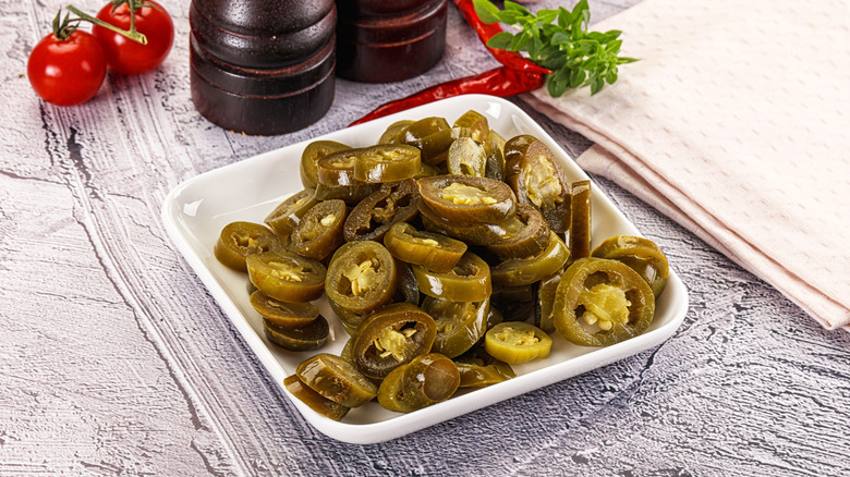 Square plate of pickled jalapenos with tomatoes, pepper mills