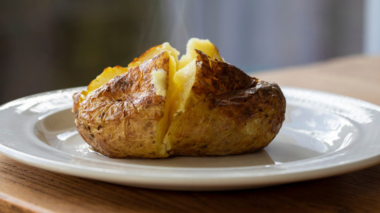 Plain baked potato cut open and steaming on a white plate