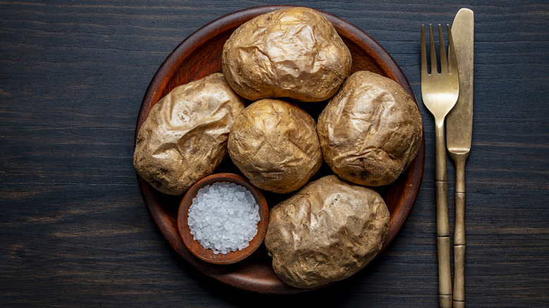 Several baked potatoes on a wooden plate sat on a table