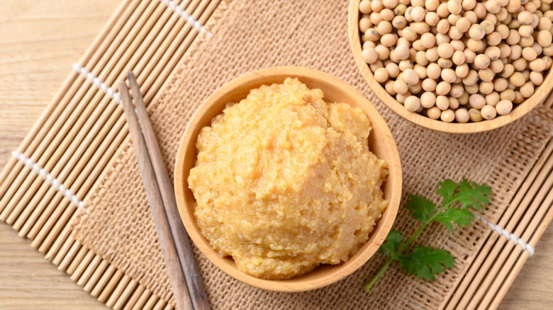 Miso paste in a wooden bowl next to a bowl of soybeans