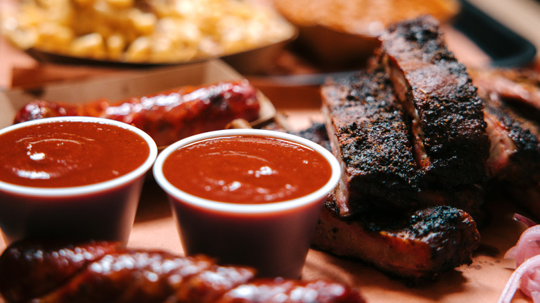Barbecued meats with two small tubs of barbecue sauce