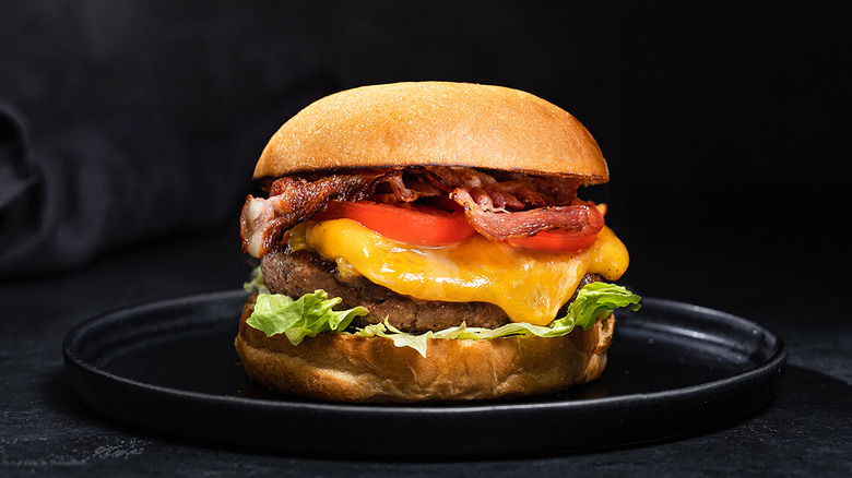 A Bacon Cheeseburger with cheese, tomatoes, and lettuce on it on a black plate