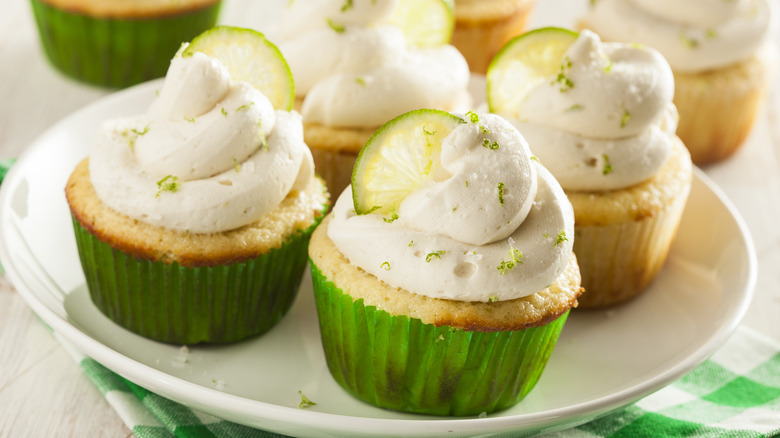 Cupcakes in green liners on white plate with white icing, lime slices