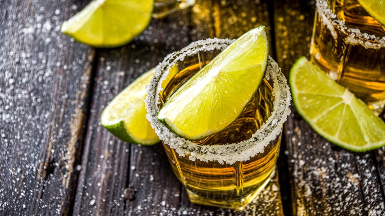 Shot glass on dark wood with tequila, lime slice, salted rim