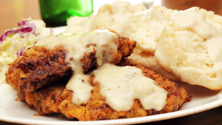 Chicken-fried steak with white gravy on a white plate with biscuits