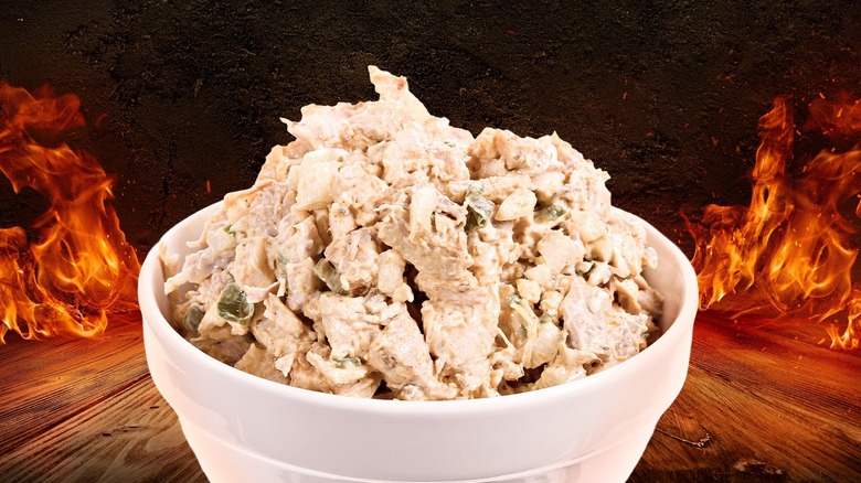 a bowl of chicken salad on a wooden surface with fire in the background
