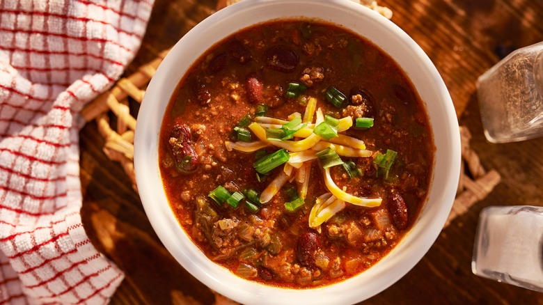 Overhead view of bowl of chili topped with cheese and green onions