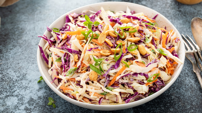 Asian-style coleslaw with cabbage, carrots, peanuts, and green onions in a bowl near silverware.