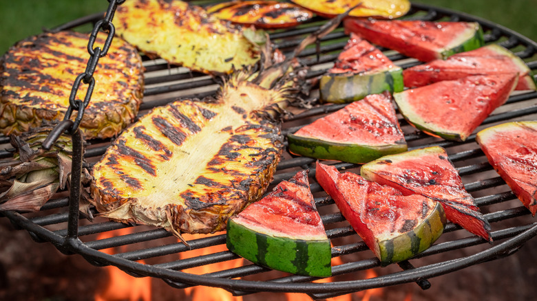 Watermelon and pineapple slices on a grill over flames