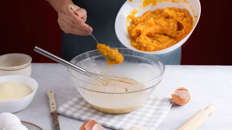 Hand spooning pumpkin puree into bowl with cream mixture