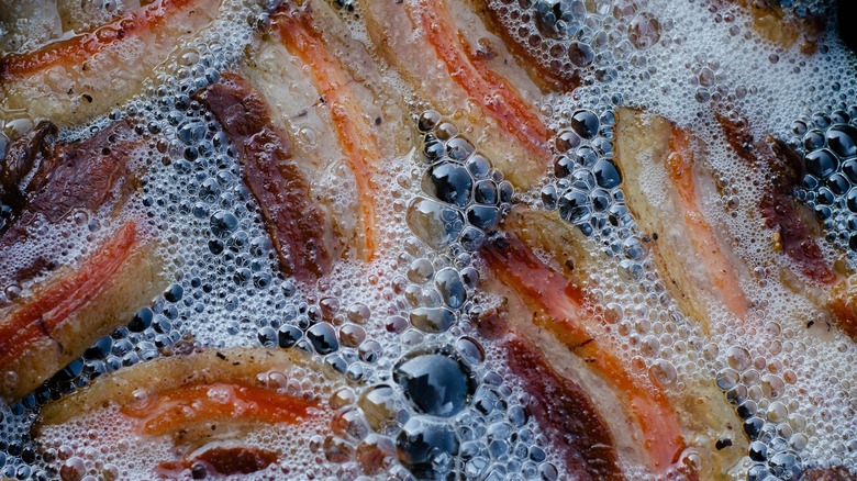 Close-up of pieces of bacon frying in a lot of their bubbly fat