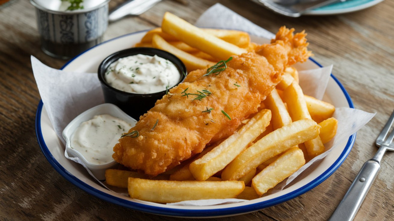 Plate of fried fish and chips with two small bowls of tartar sauce.