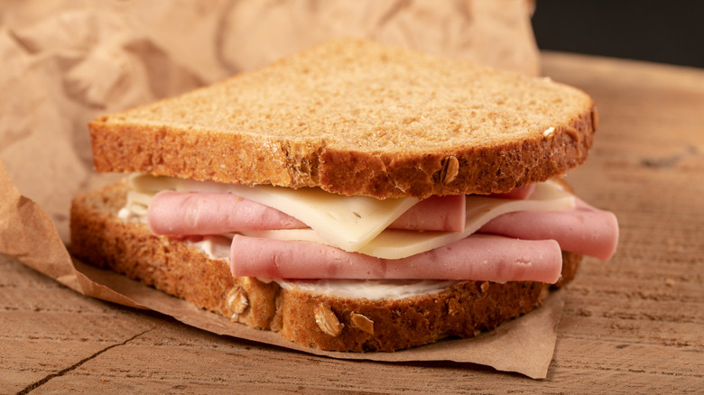 A ham and cheese sandwich on butcher paper on a wooden board