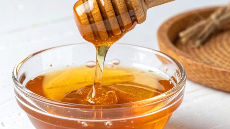 Honey in a small glass bowl being drizzled with a wand.