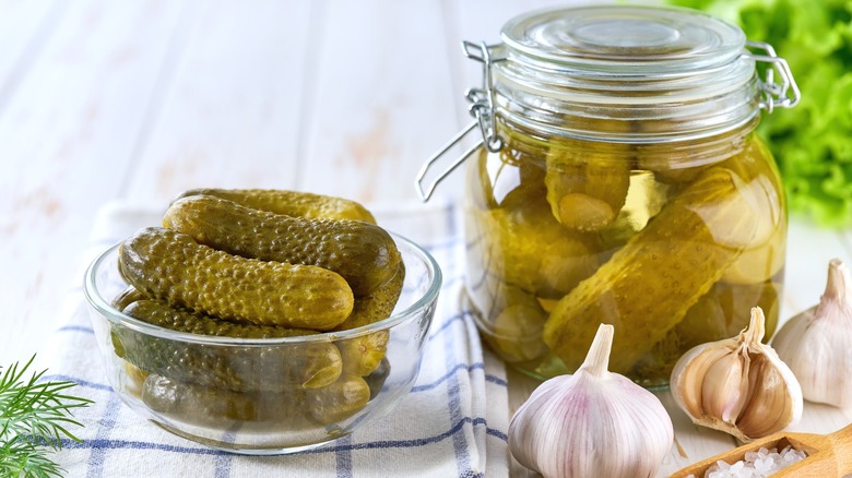 A jar of pickles next to a glass bowl of same.