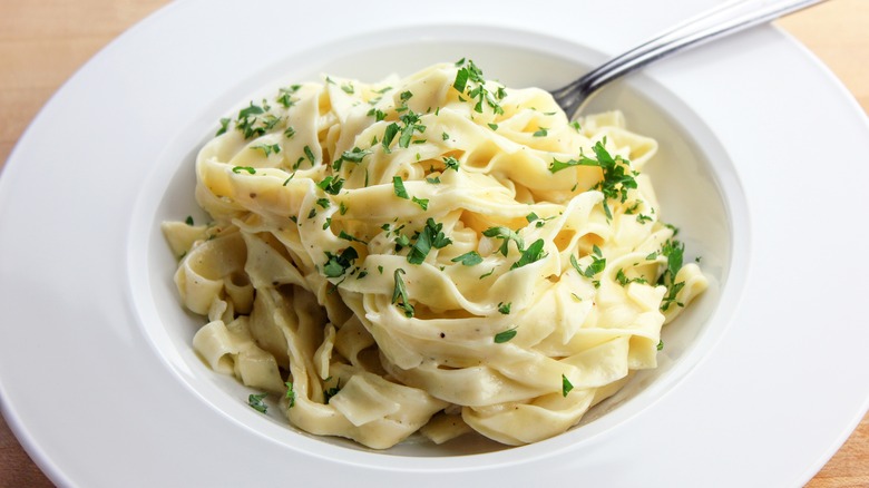 White bowl of fettuccine alfredo with chopped parsley