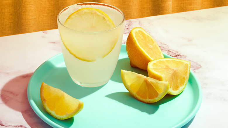 Small glass of lemonade and sliced lemons on turquoise plate