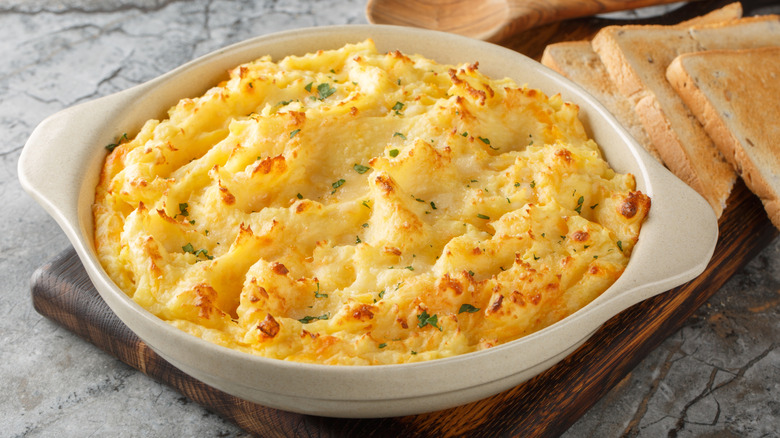 Fluffy delicious baked mashed potatoes with cheese, cream and butter close-up in baking dish on table.
