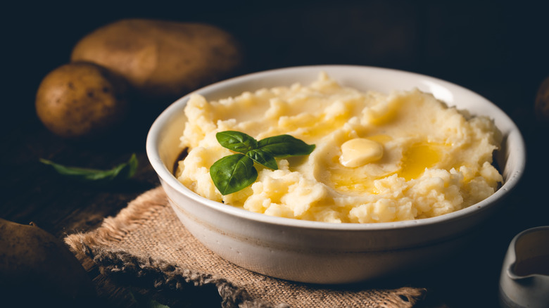 White bowl of mashed potatoes with melted butter and basil leaves