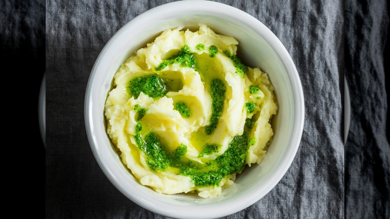 White bowl of mashed potatoes with pesto sauce
